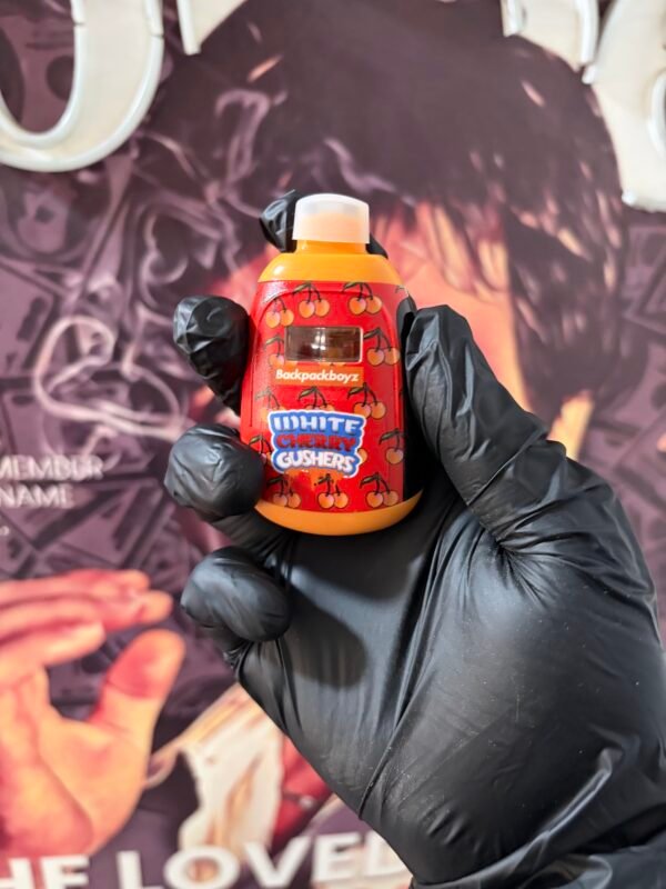 WHITE CHERRY GUSHERS 5 Orange cherry Gummies bottle labeled 'White Cherry Gummies' held by gloved hands in front of a purple backdrop background.